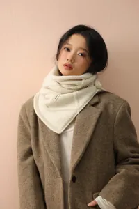 Detailed close-up of cream chunky knit snood scarf with button and small brand tag