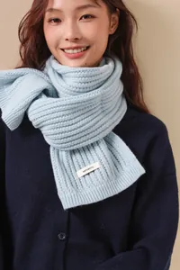Dettaglio dell'etichetta 100% lana sulla sciarpa a maglia grossa in azzurro chiaro