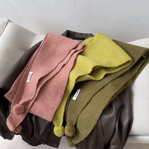 Detail of knitted winter scarves with cute pom-poms and brand label on leather jacket