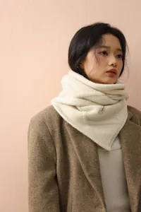 Detail of cream cable knit scarf with button and brand label on a brown wool coat