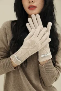 Detail of beige merino wool cable knit gloves featuring a silver brand logo plate