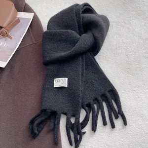 Detail of a black knit wool scarf featuring thick tassels and a woven brand label