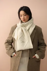 Detail of cream knit scarf featuring diamond pattern, brand tag, and button closure