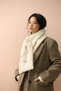 Detail of cream cable-knit scarf with woven texture and button accent for winter warmth