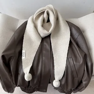 Detail of cream knit scarf with fluffy pom-poms and KN STUDIO label on a leather jacket