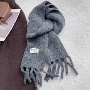 Detail of dark grey knit wool scarf showing fringe and woven brand label on coat