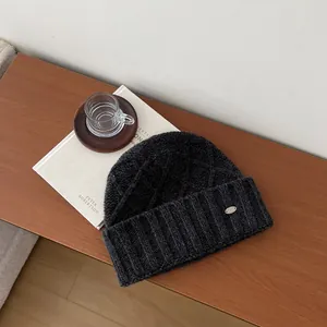 Detail of grey wool knit beanie featuring cable pattern and small oval metal logo