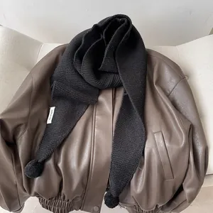 Detail of black knitted scarf with soft pom-poms on a dark leather jacket for winter warmth