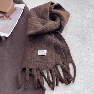 Close-up of thick brown wool scarf texture with fringe detail and brand woven label