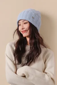 Close-up of light blue knit wool beanie showing cable texture and metal logo detail