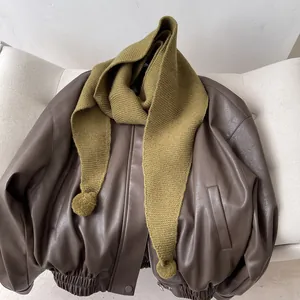Close-up of olive green knitted triangular scarf with decorative matching fur pom-poms