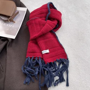 Detail of red knit scarf featuring blue tassel edges and a white brand label