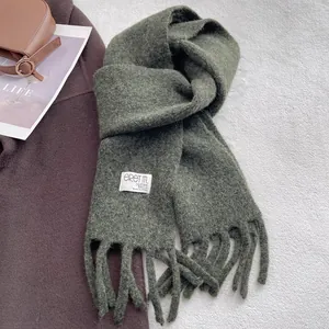 Close-up of dark green wool scarf with fringe and brand label on white furry background