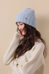 Detail of light blue wool knitted beanie with diamond pattern and metal logo tag