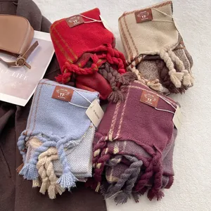 Thick plaid knit scarves with large tassels in red, beige, and blue shown on brown coat