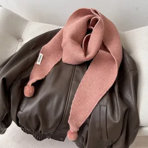 Detail of pink knitted scarf with pompom trim and KN STUDIO label on leather jacket