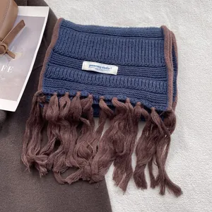 Close-up of vintage blue knit scarf with brown fringe and brand label on soft rug