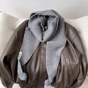 Detail of grey chunky knit hooded scarf featuring soft faux fur pom-poms on leather jacket