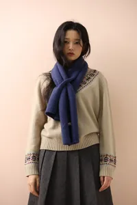 Detailed close-up of blue cable knit scarf with button and branding tag on beige sweater