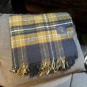Détail d'une écharpe à carreaux moutarde et bleu marine avec des bords frangés