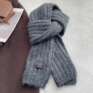 Close-up of dark grey knitted scarf showing ribbed texture and brand label detail