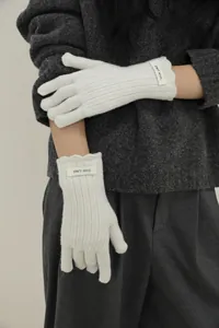 Close-up of white wool knitted gloves with elegant ruffled cuffs and label detail