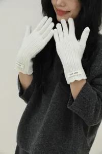 Detailed close-up of white wool knit gloves featuring ribbed texture and ERET-WOOL label