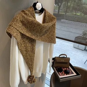 Detail of tan knit wool scarf with soft pom-pom fringe accent on a white sweater