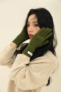 Detail of forest green ribbed wool glove with brand label on a soft beige background
