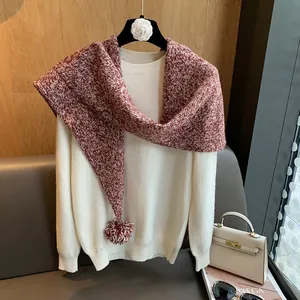 Detalle de bufanda de lana de punto burdeos y blanco con pompones sobre un suéter crema