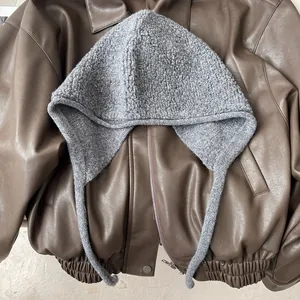 Détail de la cagoule en laine grise avec cache-oreilles sur fond de veste en cuir vintage