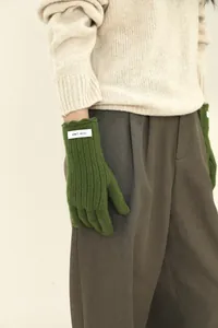 Detail of green ribbed wool knit gloves with a branded woven label on the cuff