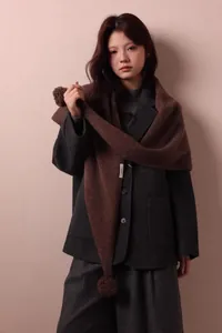Detalle de bufanda triangular de lana marrón oscuro con pompón y tejido de punto grueso