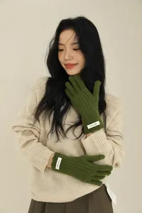Detail of dark green ribbed wool gloves with ERET-WOOL logo patch on a casual outfit