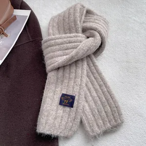 Macro detail of beige ribbed knit scarf texture with a woven brand label for winter warmth
