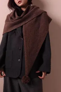 Detalle de chal triangular de lana marrón con pompón sobre una chaqueta de tweed gris