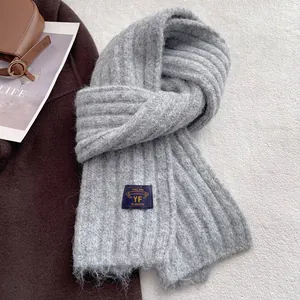 Close-up of grey chunky knit scarf with premium ribbed texture and navy woven patch detail