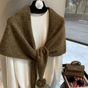 Detailed knit texture of a heavy dark brown wool shawl featuring a soft pom-pom accent