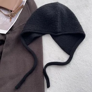 Détail d'une cagoule en laine bouclée noire avec cache-oreilles et liens de serrage