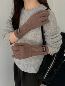 Detail of dark brown knitted long gloves with ribbed texture and brand logo patch
