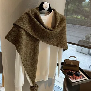 Close-up of heavy knit wool triangle shawl with decorative pom-poms and fine stitch texture