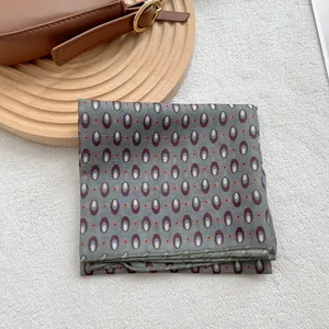 Gray silk square scarf with geometric burgundy oval patterns on white textured carpet