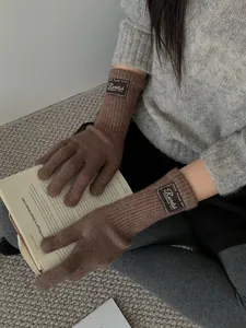Close-up of dark brown knitted gloves featuring vintage labels and extended ribbed cuffs