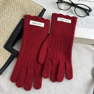 Detailed macro view of dark red wool knit gloves with scalloped cuffs and brand label