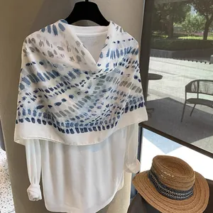 Detail of blue ink splash print scarf styled with a straw hat for a summer beach look