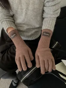 Detail of warm brown knitted gloves with leather brand patch on long ribbed cuffs