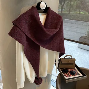 Detail of burgundy wool knit shawl with decorative pom-poms over a white sweater