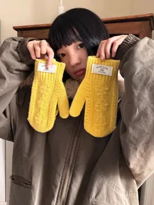 Détail de moufles en maille torsadée jaune vif en laine mélangée avec étiquette de marque