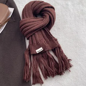 Detail of deep brown knit scarf showing thick fringe edges and designer fabric label