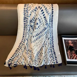 Close-up of blue tie-dye cotton linen shawl featuring soft fringe details on a leather seat